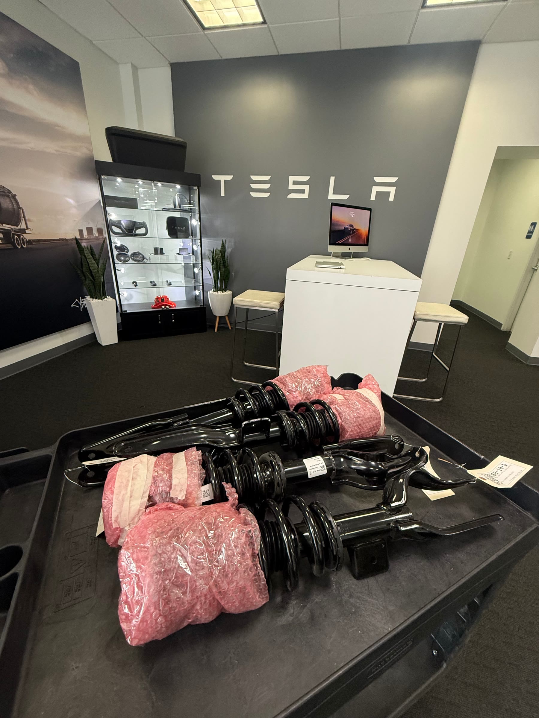 Genuine Tesla Highland and Juniper spring and damper assemblies on a cart at the Tesla parts counter